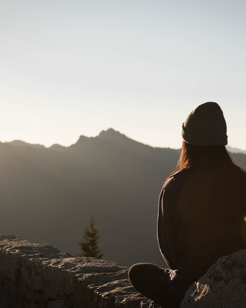 A person sitting on a rock at sunrise, looking out over mountains